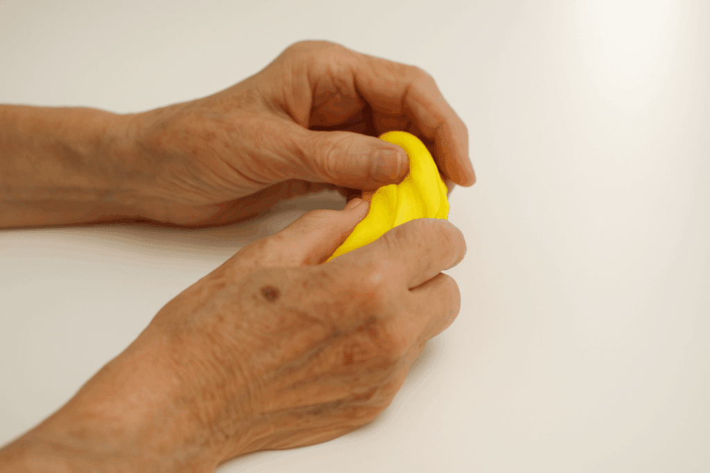 Hände einer älteren Person beim Kneten gelber Knete – ergotherapeutisches Training in der Geriatrie